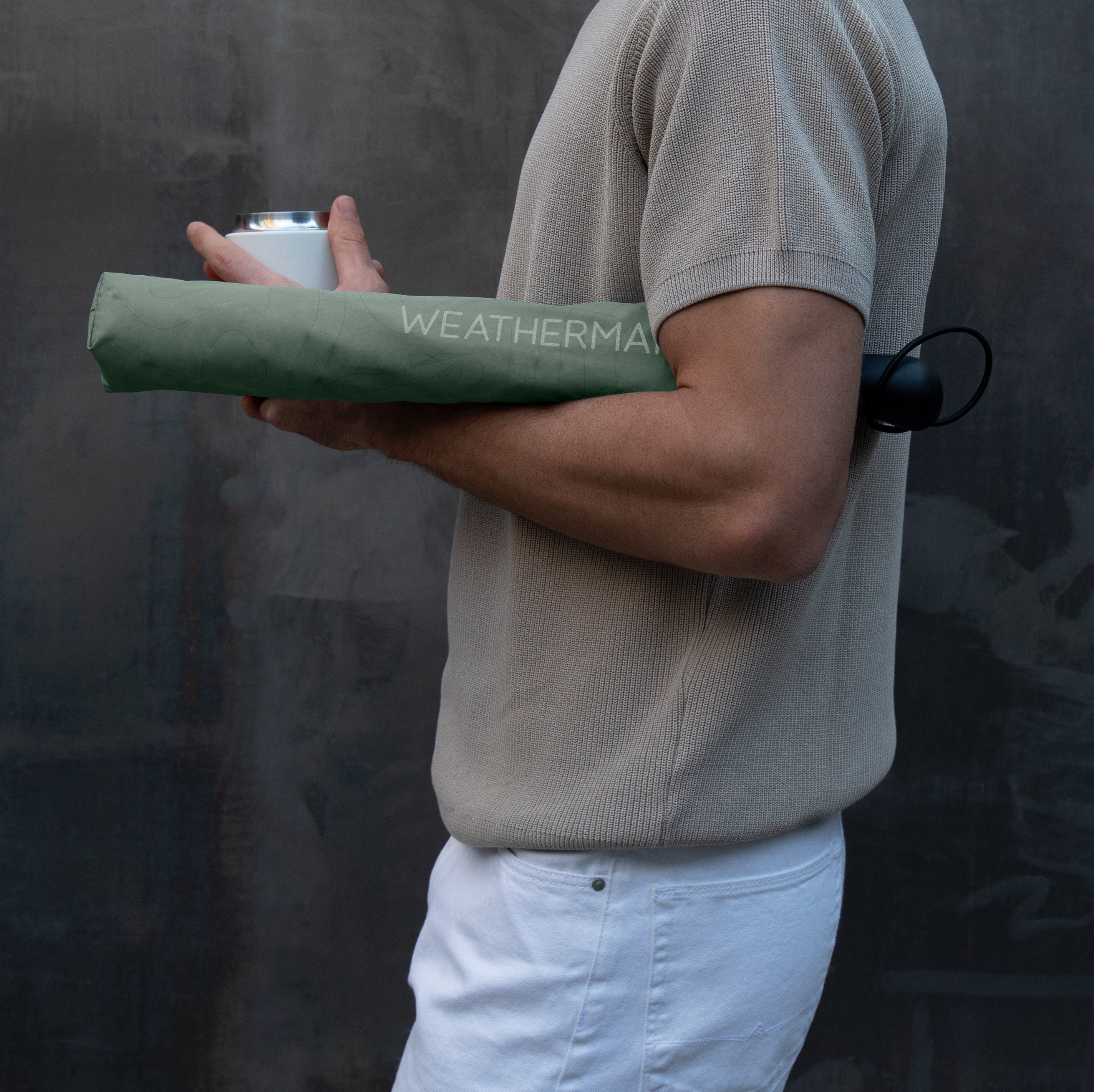 Man holding a mug and Weatherman Collapsible Umbrella in sage green.